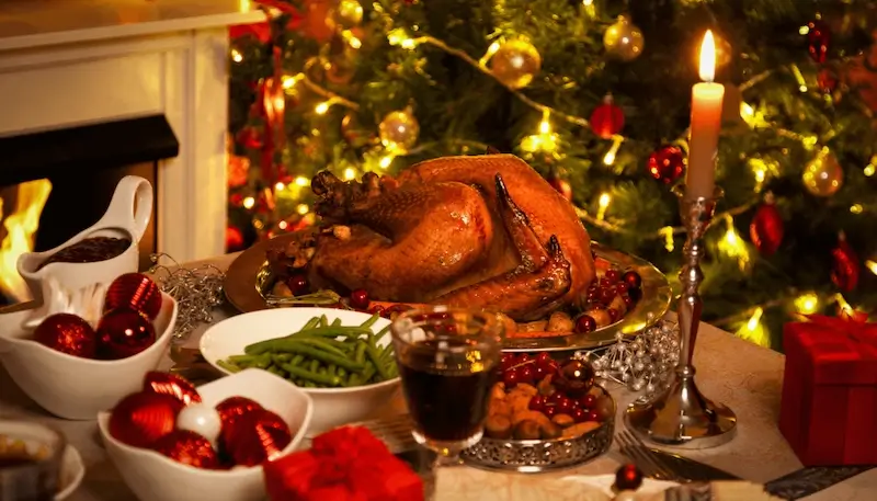 A roast turkey on a Christmas table with other dishes around and wine glasses