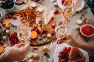 Picture of a Christmas table with people cheering with Champagne glasses. Plates full of turkey and Christmas dishes in the background.