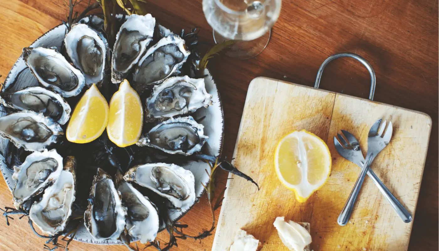 A platter of oysters on a table, with some lemon and wine glasses next to it