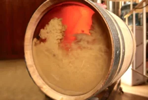 A wine barrel with a see-through bottom where you can see white wine and wine lees being stirred