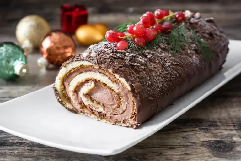 A chocolate Yule Log on a plate on a table with Christmas decorations
