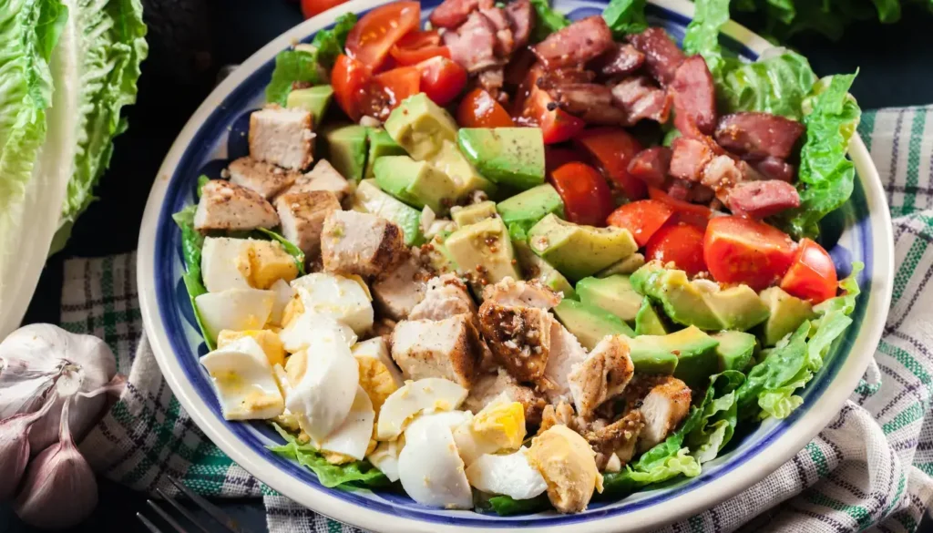 A Cobb salad in a bowl with hard-boiled eggs, chicken, avocado, tomatoes and bacon