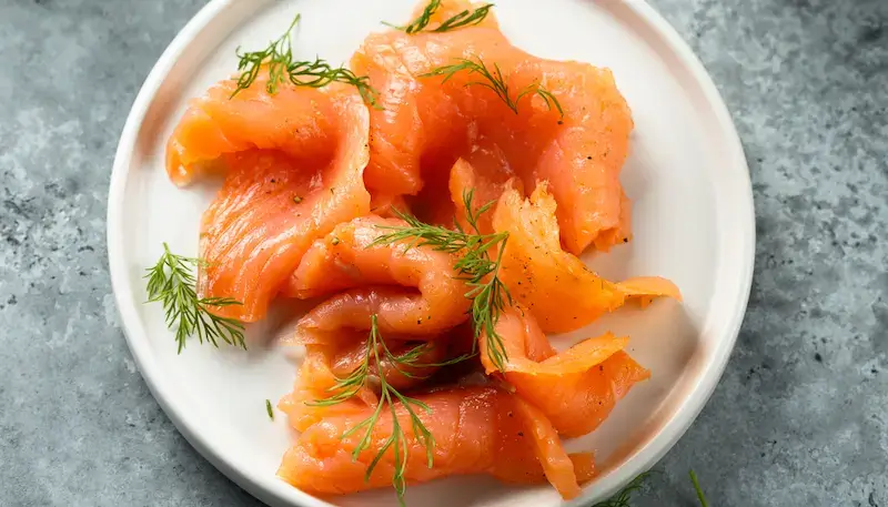 Smoked salmon with some dill on top of it, nicely placed in a plate.