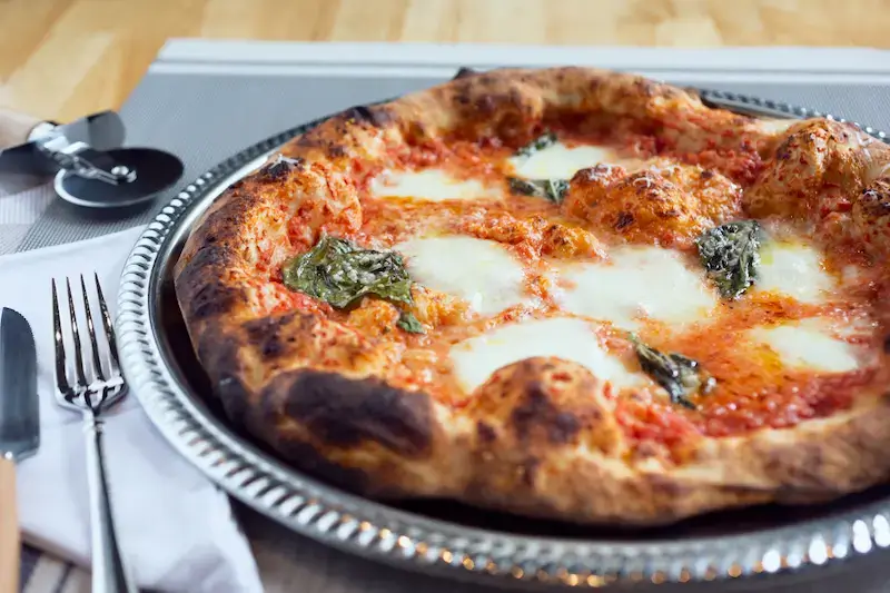A Margherita pizza in a plate on a table with cutlery