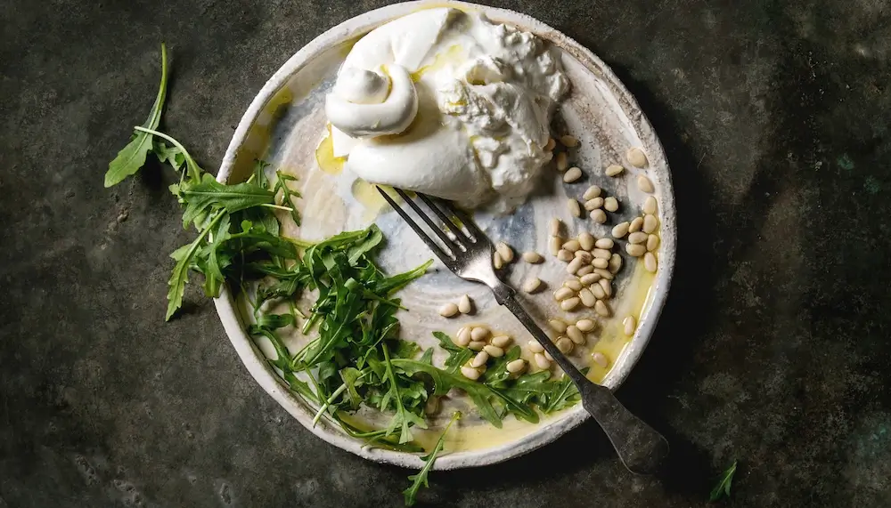 A plate with a creamy burrata, olive oil, rocket and pine nuts
