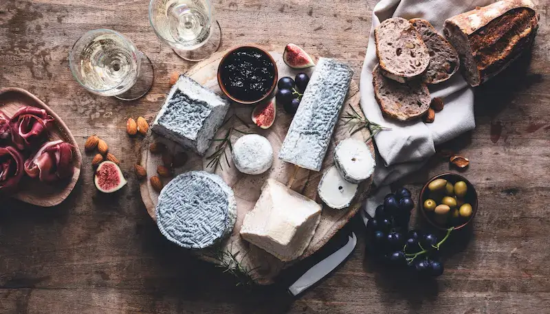 A table with a cheese board full of different types of goat's cheese, bread, figs, olives