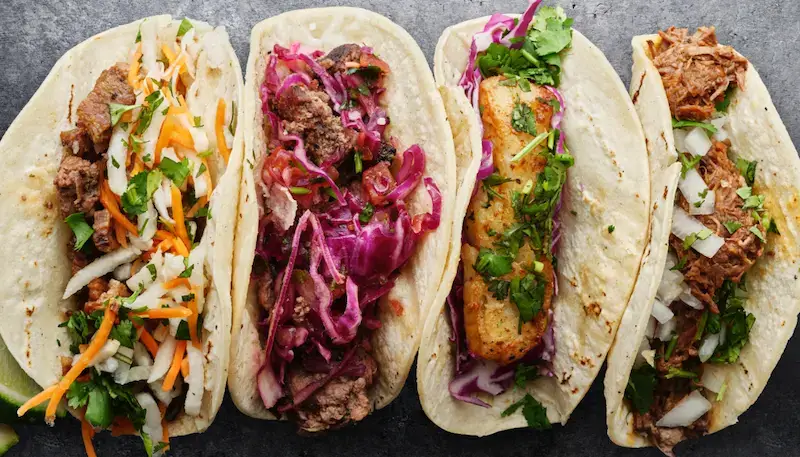 Four tacos with different fillings - pork, beef, chicken, fish, with some salad on top