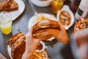 Someone holding a burger, we can see grilled cheese, fries and other comfort food in the background