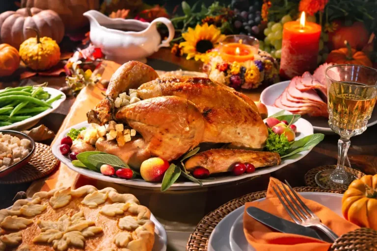 A picture showing a Thanksgiving table with a roast turkey, pies, stuffing, greens, pumpkins, ham and glasses of wine