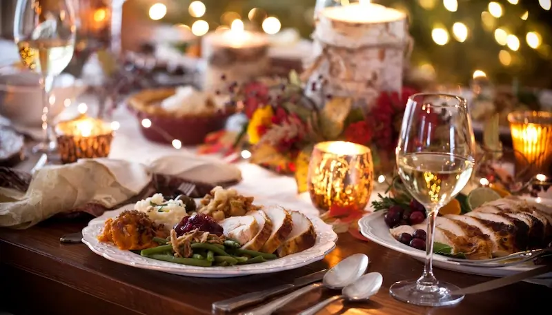 A picture showing a Thanksgiving dinner table with plates full of the different dishes - slices of turkey, cranberry sauce, stuffing, mash potatoes, gravy, along with wine glasses and a decorated table with candles etc.
