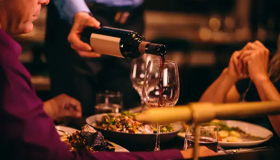 A waiter pouring red wine into a glass at a table