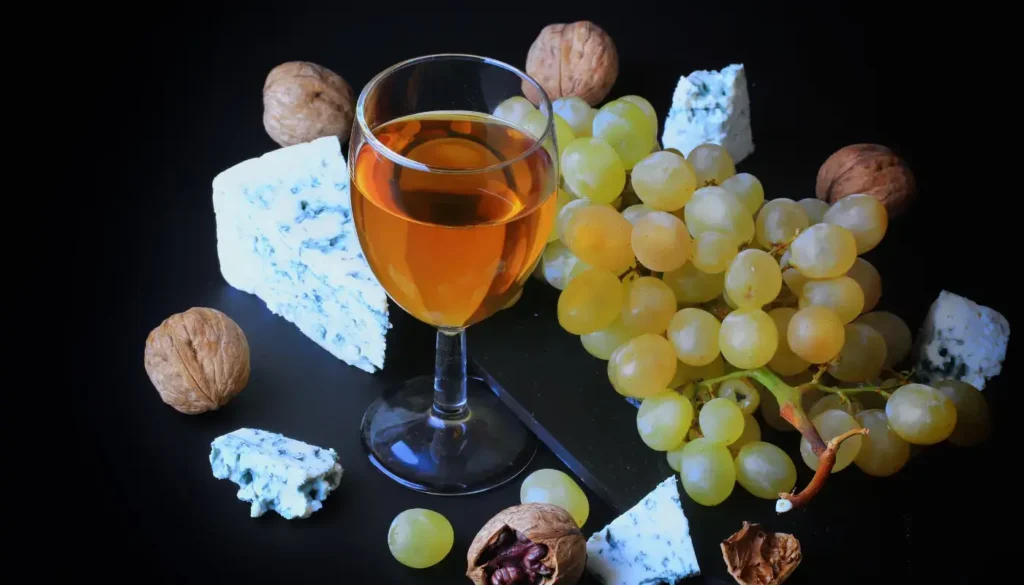 A glass of golden sweet wine with blue cheese, walnuts and white grapes