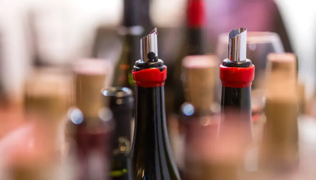 Open wine bottles fitted with metal pourers on a bar