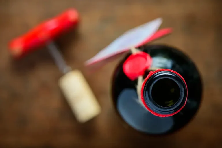 An open bottle of red wine with its cork and a corkscrew on a wooden table