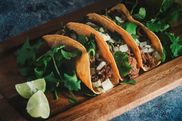 Some tacos with meat filling, onions and coriander with lime next to it