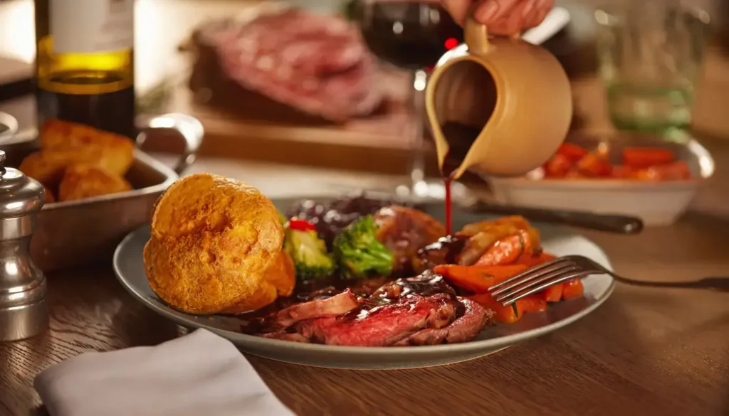 Roast beef carved on a board with Yorkshire puddings and a bottle of red wine
